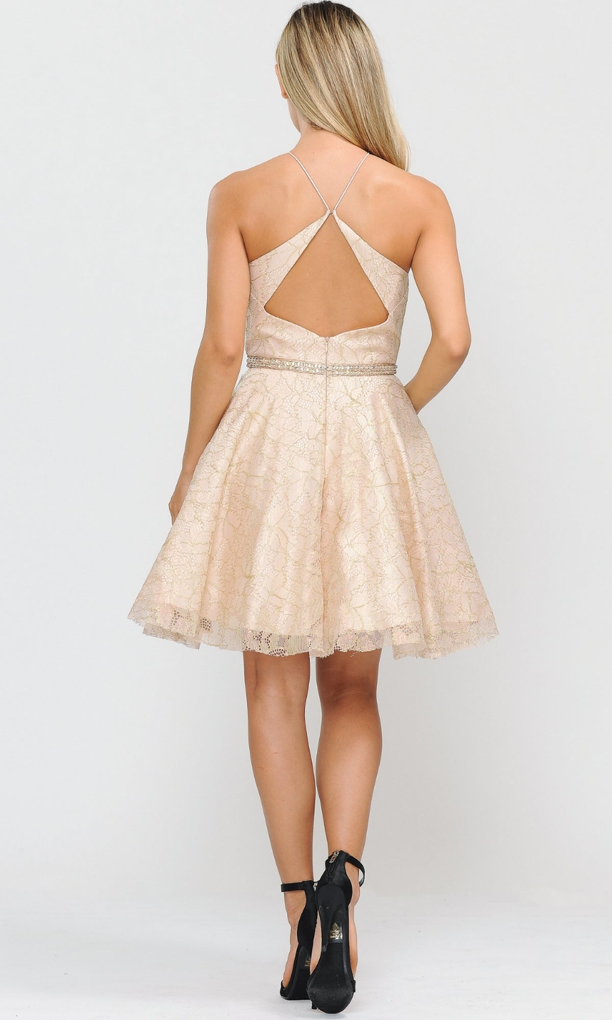 Woman stands with her back to the camera in the Glitter-Mesh Short A-Line Homecoming Dress 8506, featuring beige lace, crisscross straps, and an open back, paired with black high heels for an elegant look.
